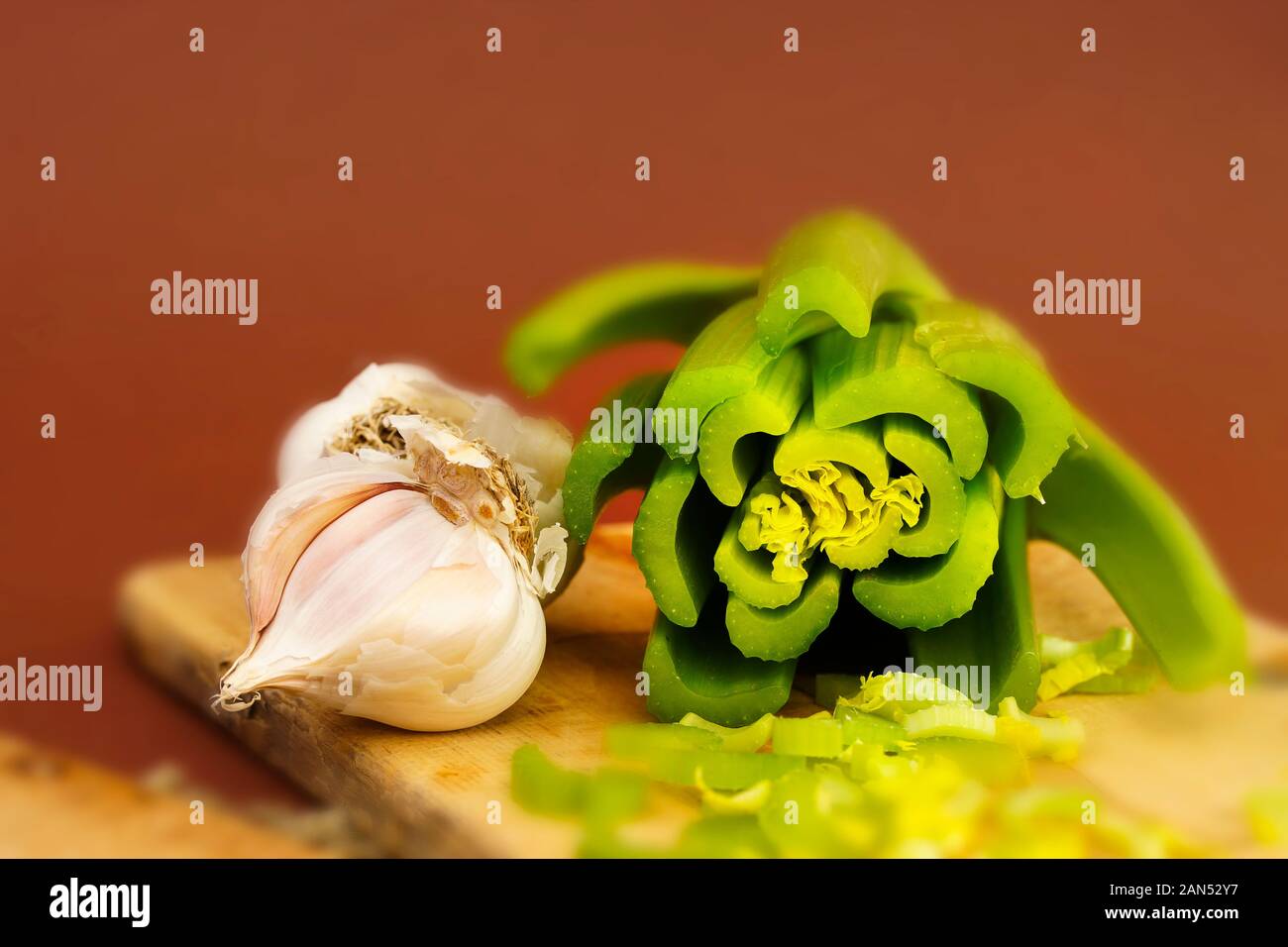 Macro horizontal photograph of garlish cloves and cut celery side by side on a cutting board. Stock Photo