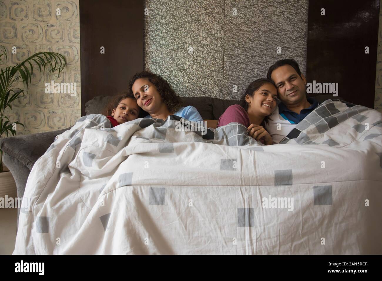 Happy family cosily sitting on the couch under a blanket at home Stock