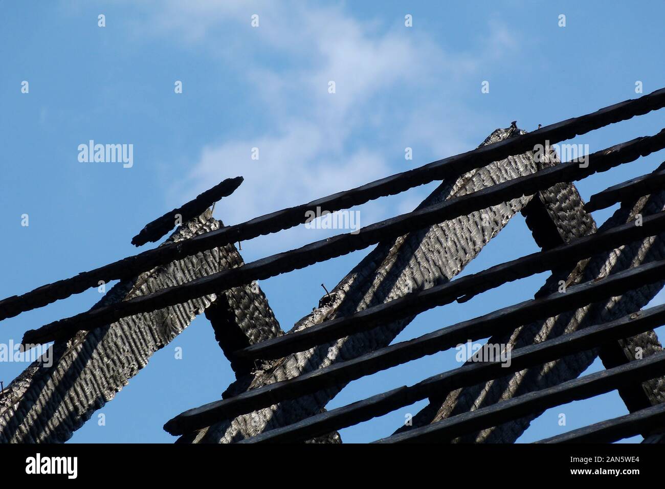 damaged exposed charred burnt black timber roof structure after house fire. abstract view of rafters under blue sky. fire safety and insurance concept Stock Photo