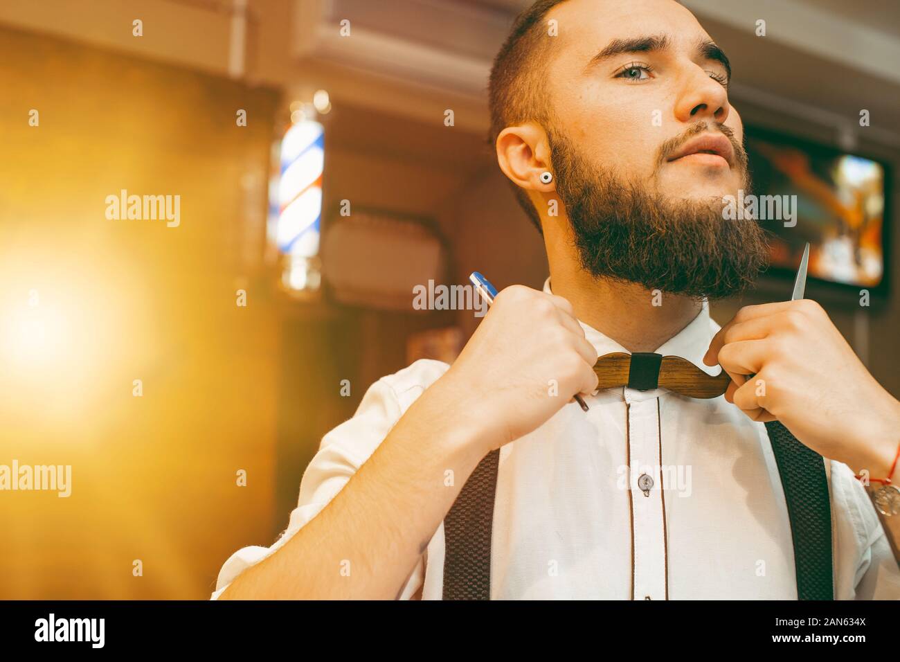 Young handsome bearded barber straightens his bow-tie. Copy space. Barber shop Stock Photo