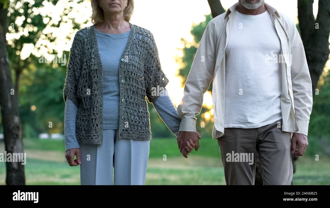 Pensive aged couple holding hands and walking forward, insecurity about ...