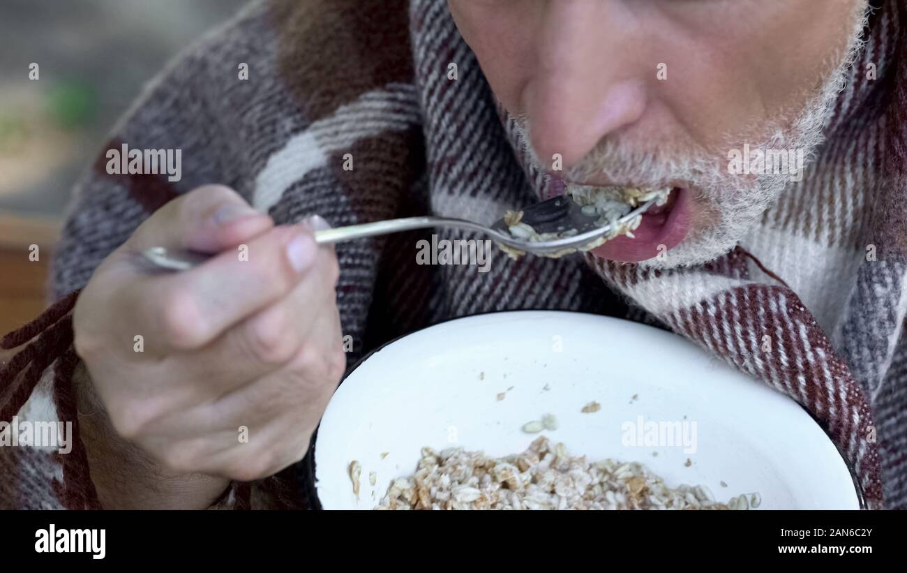 Old grandfather eating porridge, charity meals for poor pensioners, poverty Stock Photo