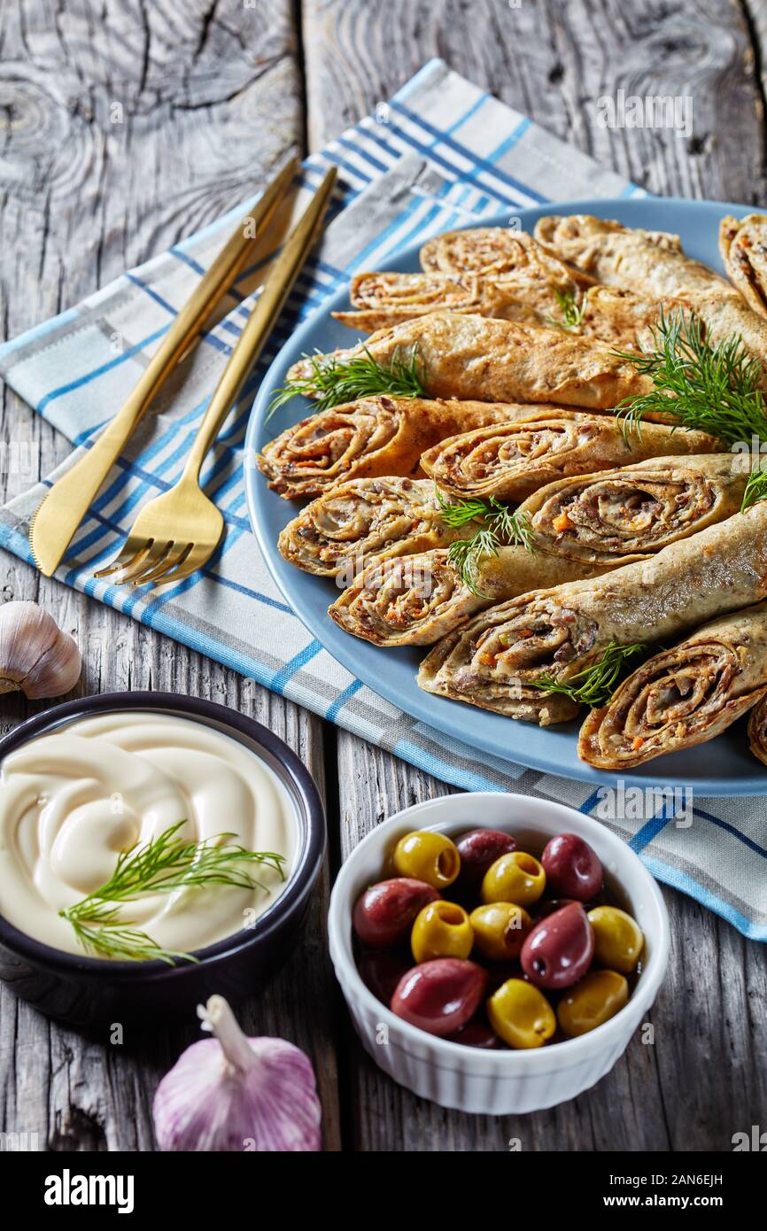 buckwheat crepes rolls with meat, vegetables and mushrooms fillings on a plate on a old rustic wooden table, vertical view from above, close-up Stock Photo