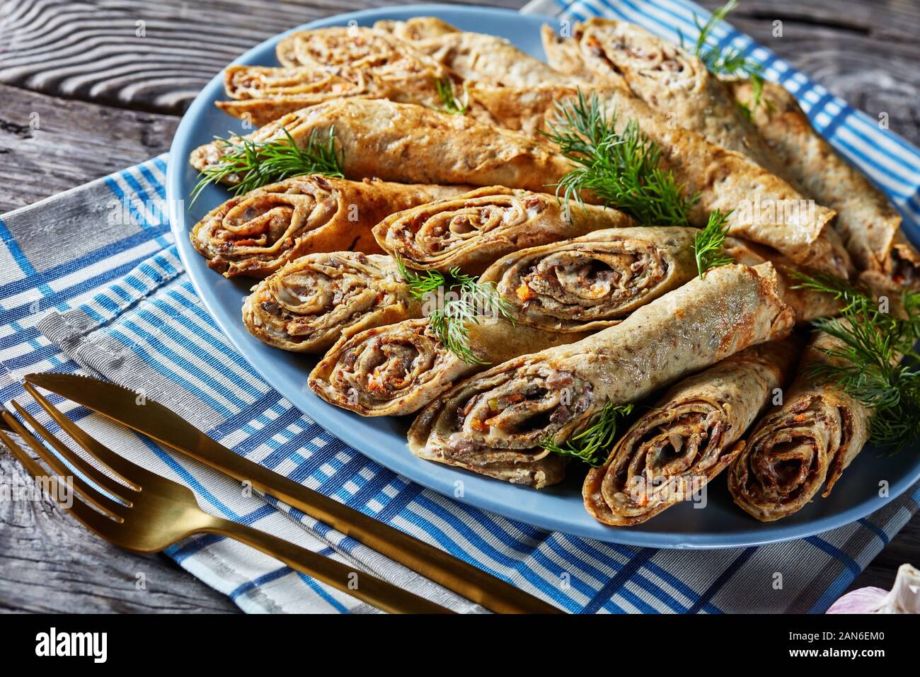 buckwheat crepes rolls with meat, vegetables and mushrooms fillings on a plate on a old rustic wooden table, horizontal view from above, close-up Stock Photo