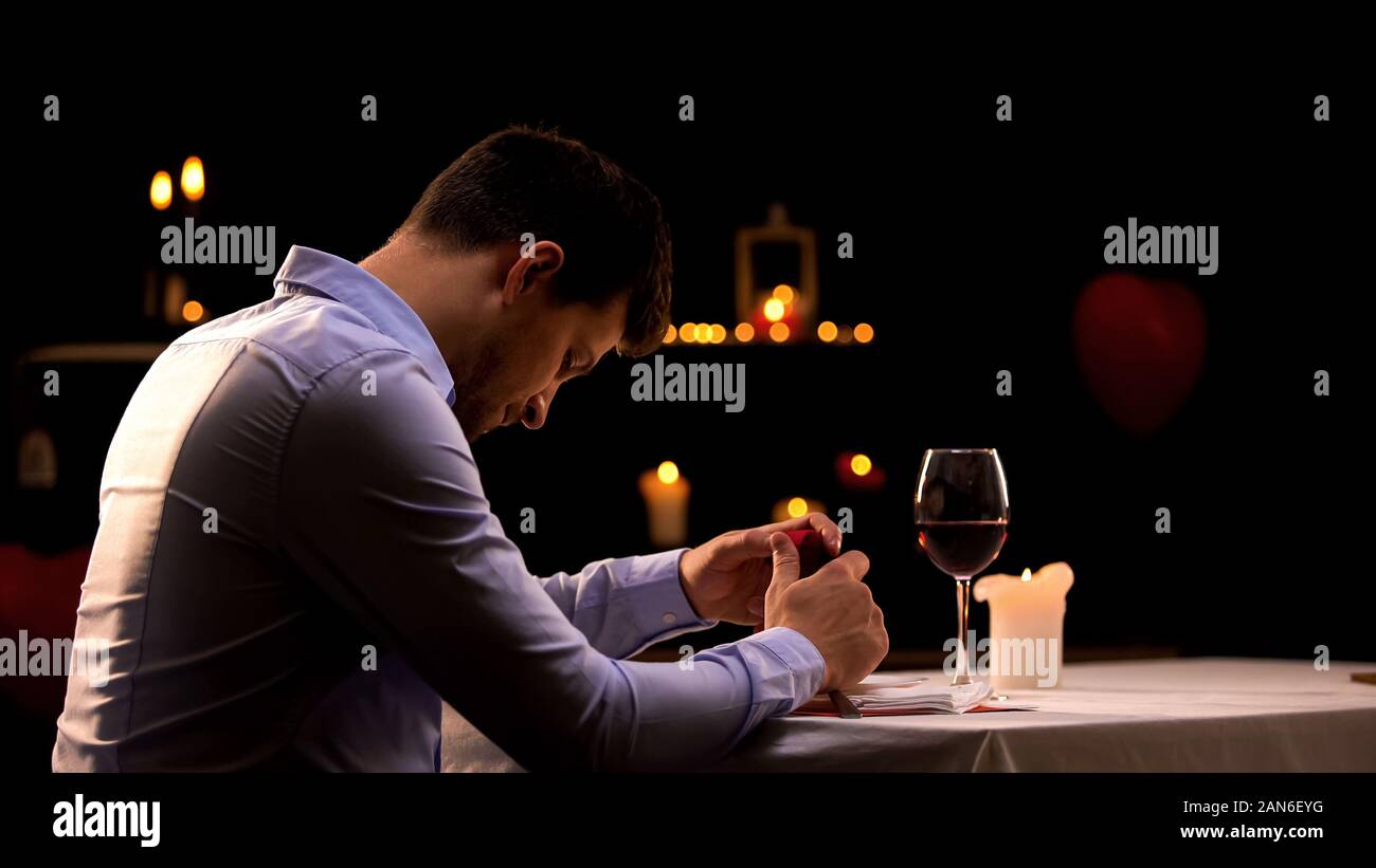 Hopeless man holding engagement ring, sitting in restaurant alone, break up Stock Photo