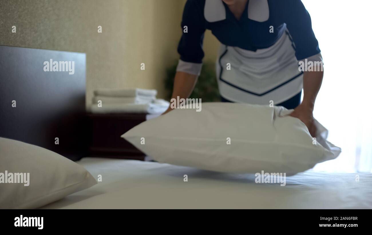 Hotel worker plumps pillows after washing bed sheets with fragrant