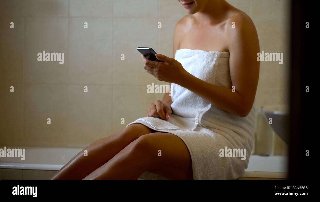 Female reading message from boyfriend at bathroom, using telephone, flirting Stock Photo