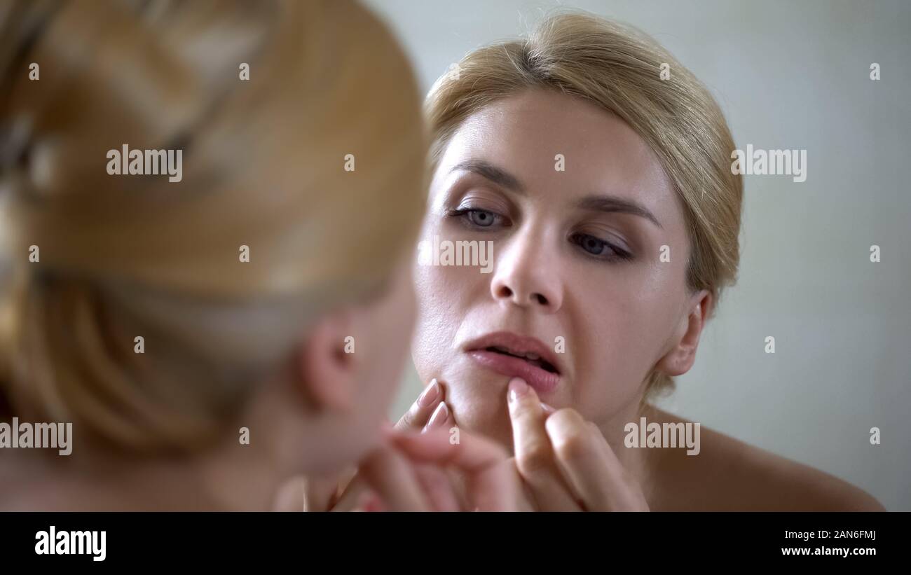 Insecure pretty lady popping pimple on skin, scrutinizing her mirror reflection Stock Photo