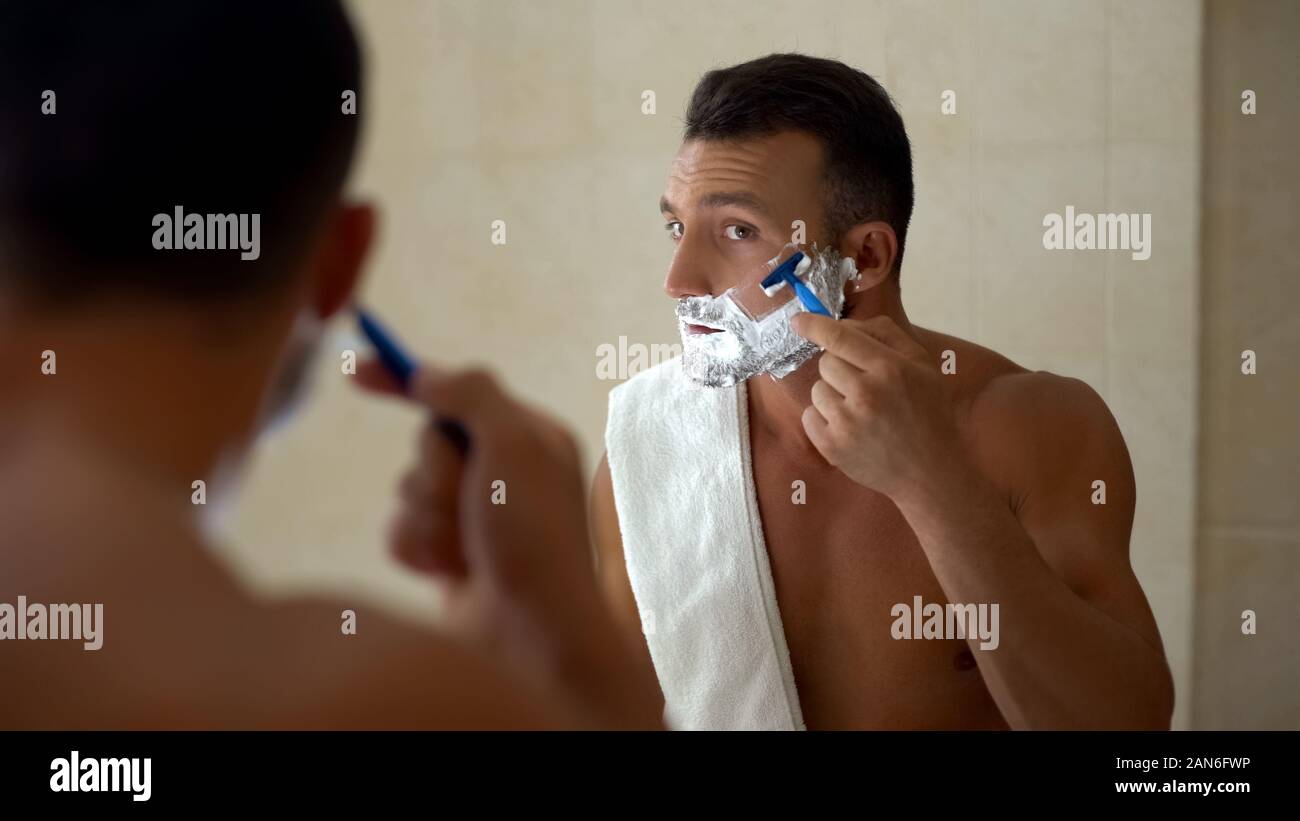 Male with foam on face using manual razor to trim and shave beard in  bathroom Stock Photo - Alamy
