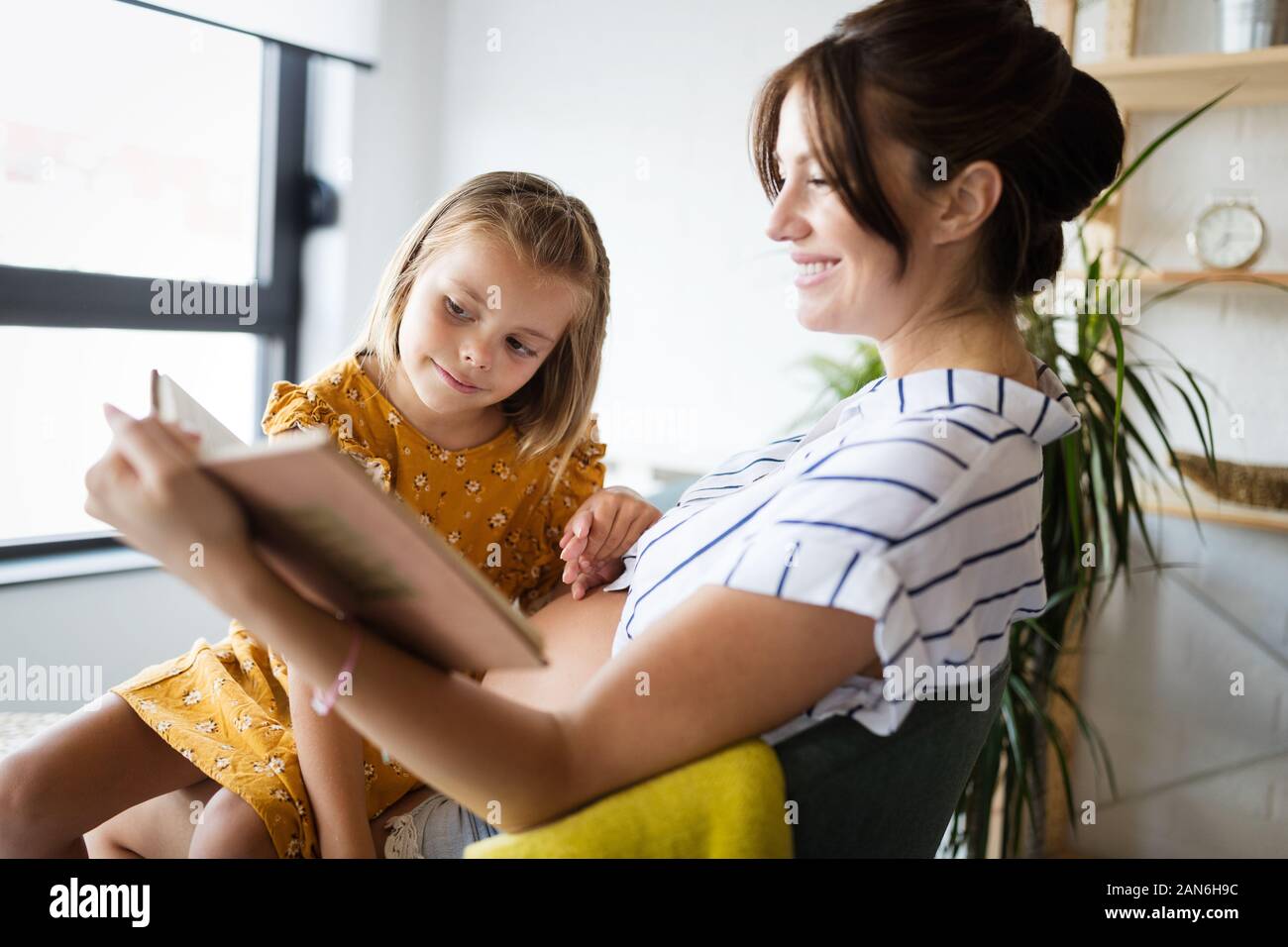 Girl and her pregnant mother reading book together. Family time Stock Photo