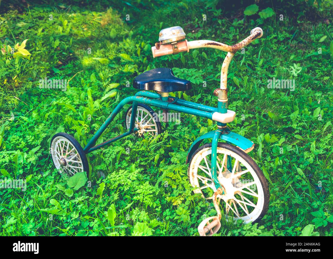 Old retro rusty children's tricycle standing on green grass Stock Photo