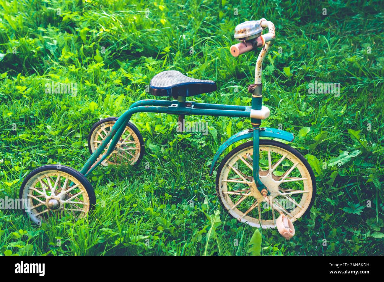 Old retro rusty children's tricycle standing on green grass Stock Photo