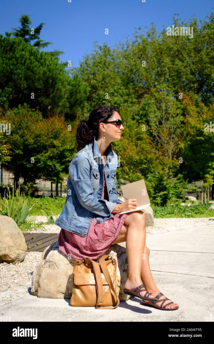 Woman sitting on a park and writing or drawing on her notebook Stock ...