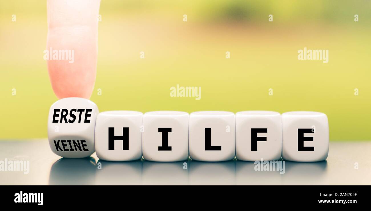 Hand turns a dice and changes the German expression 'keine Hilfe' ('no aid' in English) to 'erste Hilfe' ('first aid' in English). Stock Photo