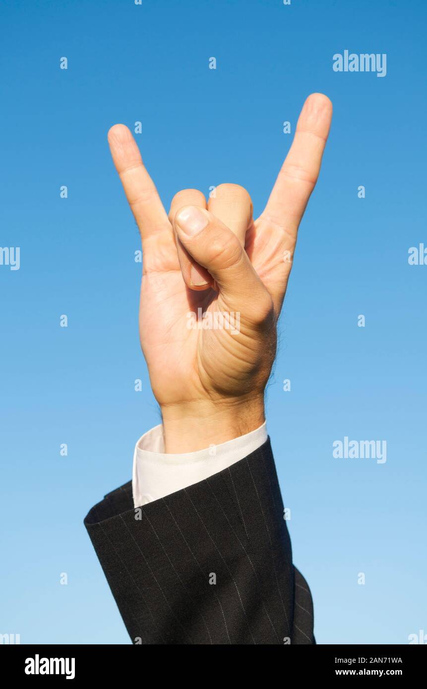 Hand of unrecognizable businessman making a rock n roll gesture outdoors in bright blue sky Stock Photo