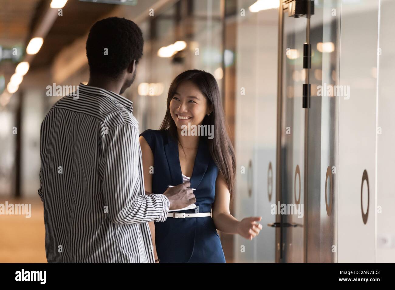 Smiling millennial multiracial colleagues talk in office hallway Stock Photo