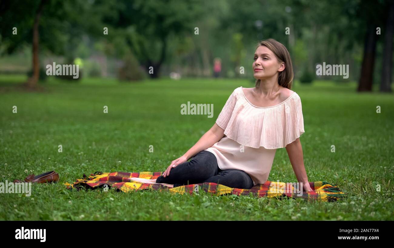 Beautiful woman sitting on plaid in park, weekend rest, breathing exercises Stock Photo