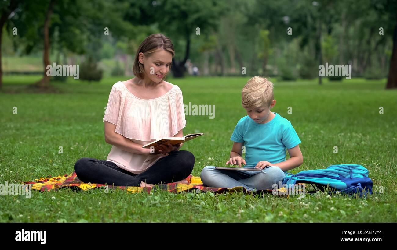 Mom reading book, son using tablet, alternative education with IT technologies Stock Photo