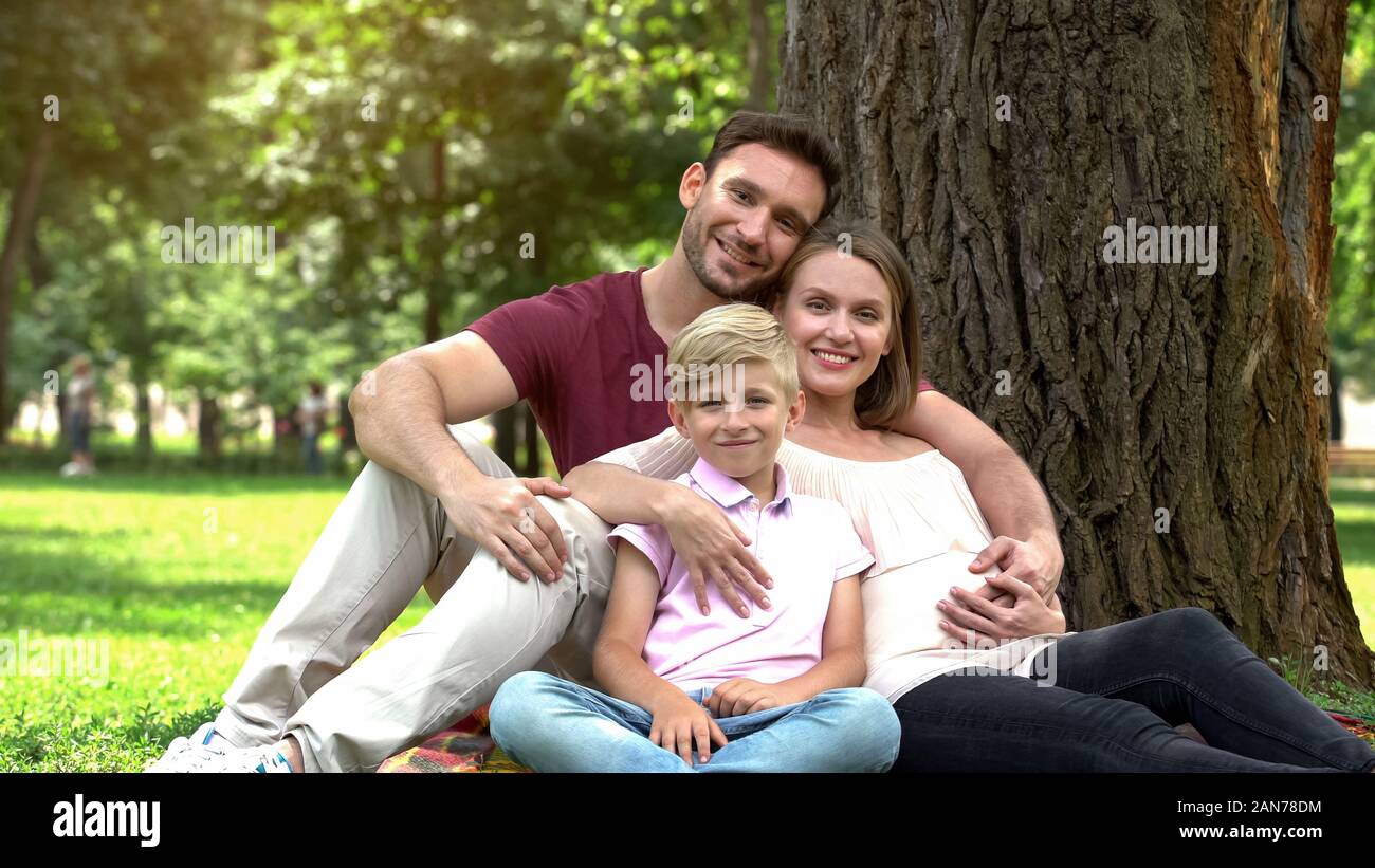 Family with son and pregnant woman looking into camera, adoption and social care Stock Photo