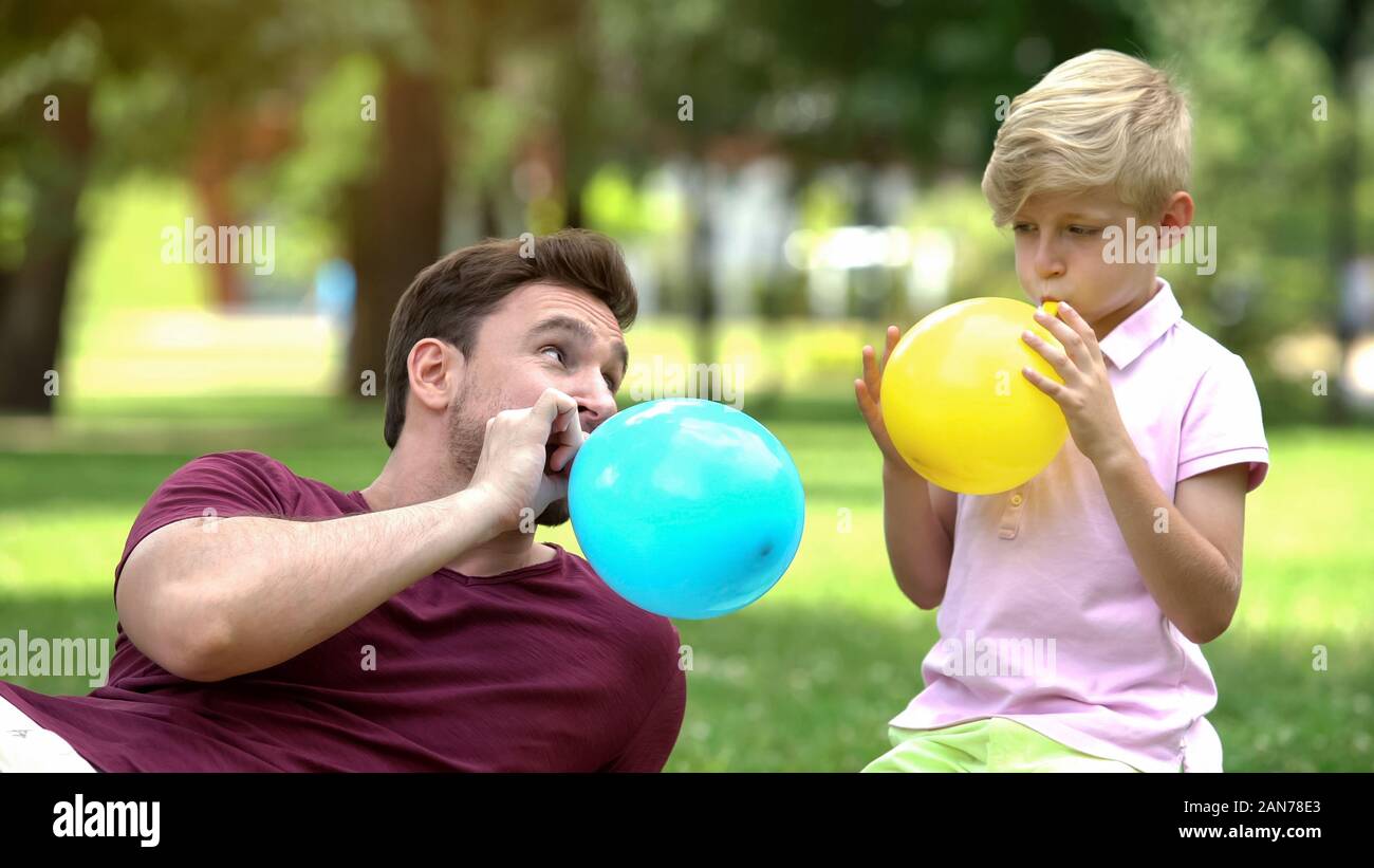 Father and son blowing up balloons, having fun together, carefree