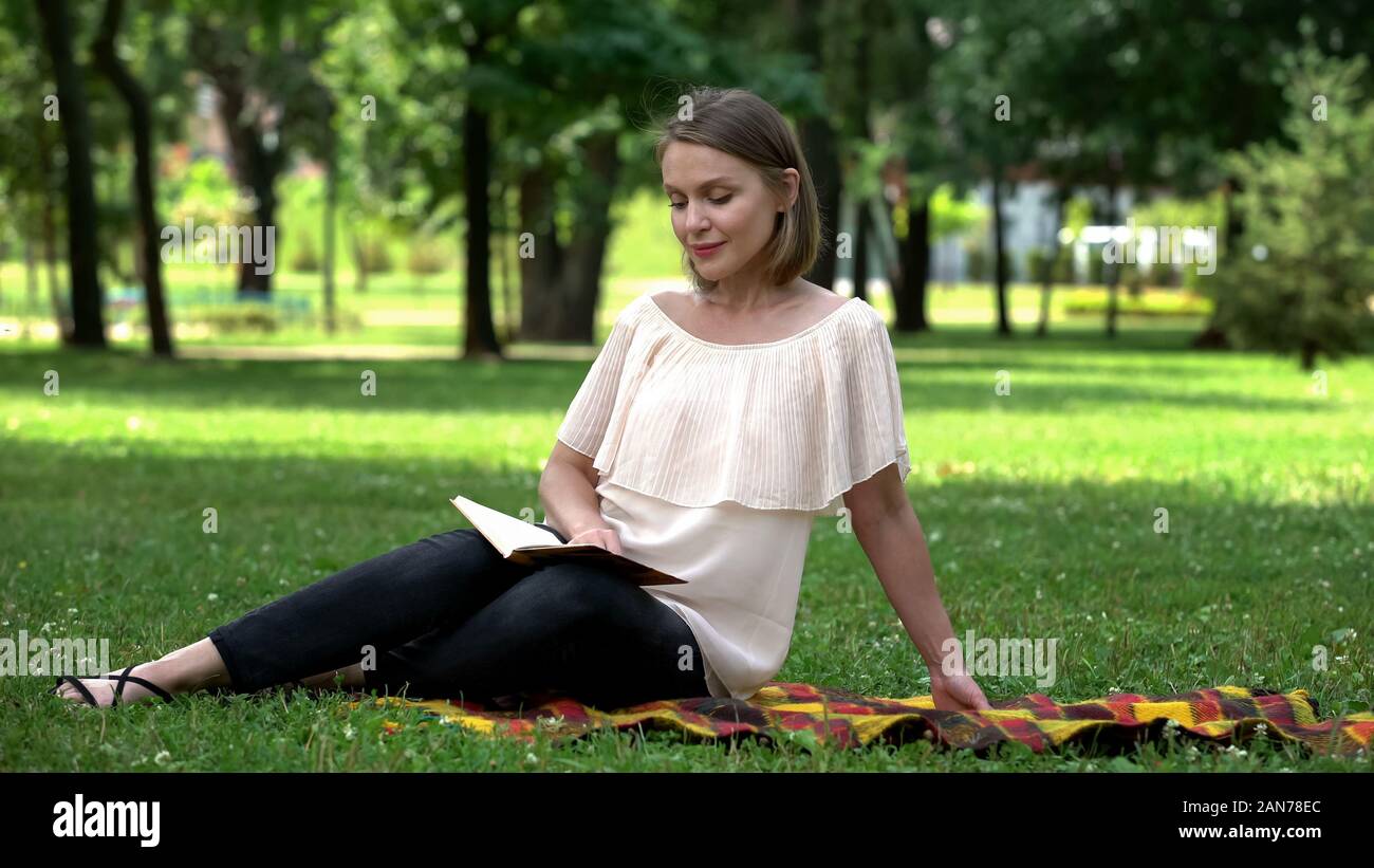 Calm pretty woman reading book about self-development in park, leisure time Stock Photo
