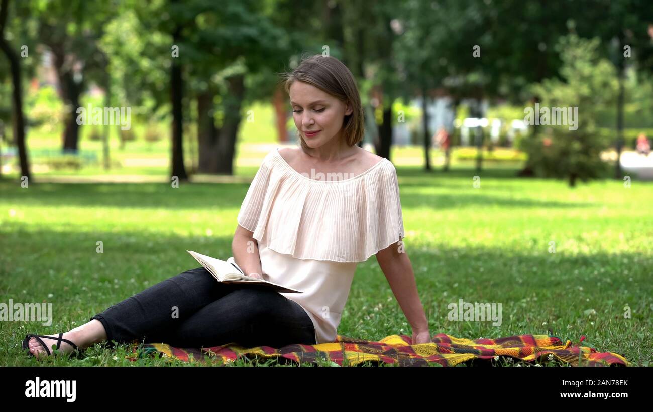 Pretty lady reading romantic novel, sitting on plaid in park, book lover Stock Photo