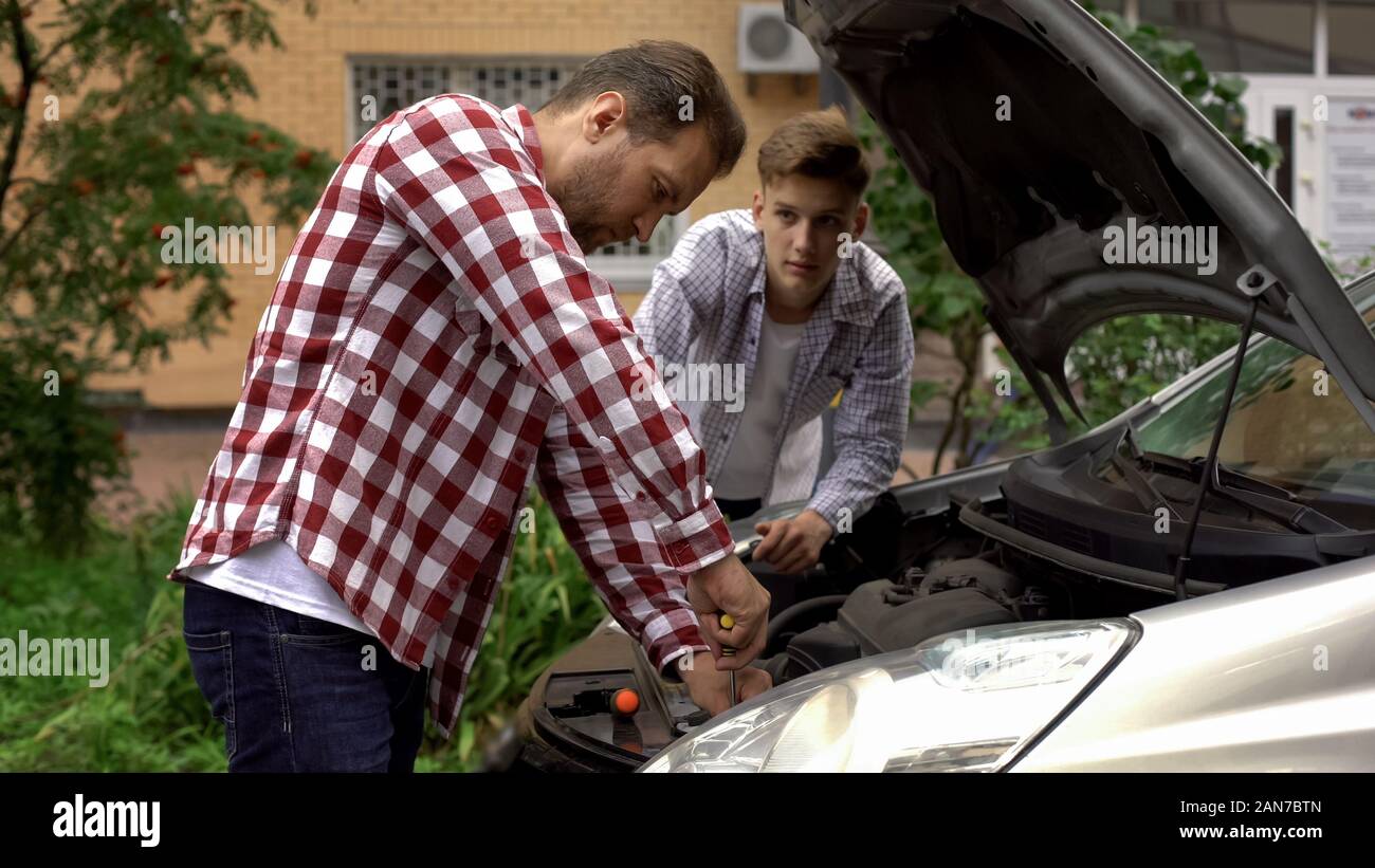Father and son fixing car, dad teaching teen boy to repair engine, role model Stock Photo