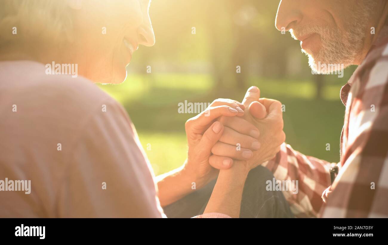 Smiling retired couple relaxing in park, holding hands and talking about love Stock Photo