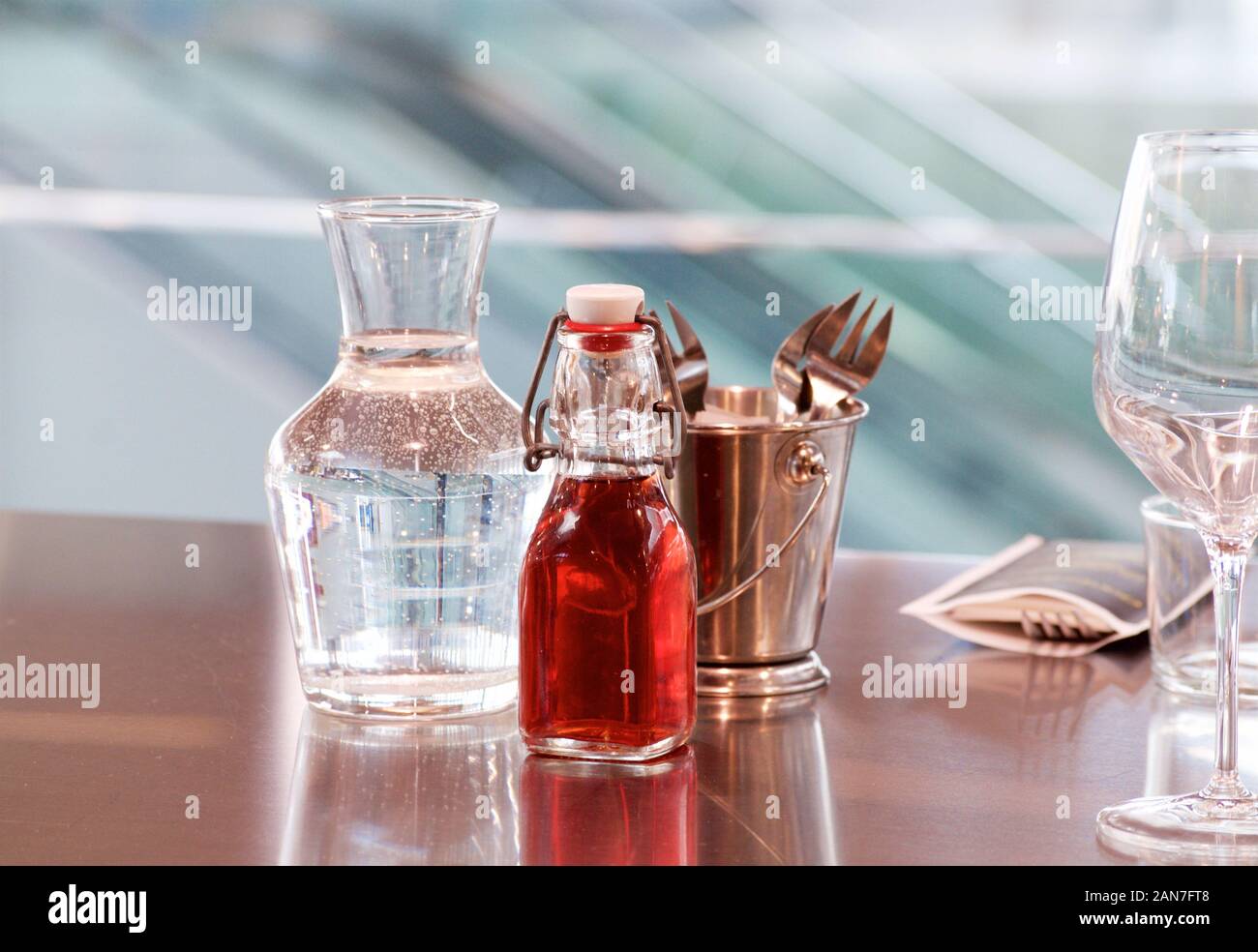 A decanter of water, a bottle of red grape vinegar and a bronze bucket with Cutlery on the smooth mirror surface of a table at a fish market in France Stock Photo