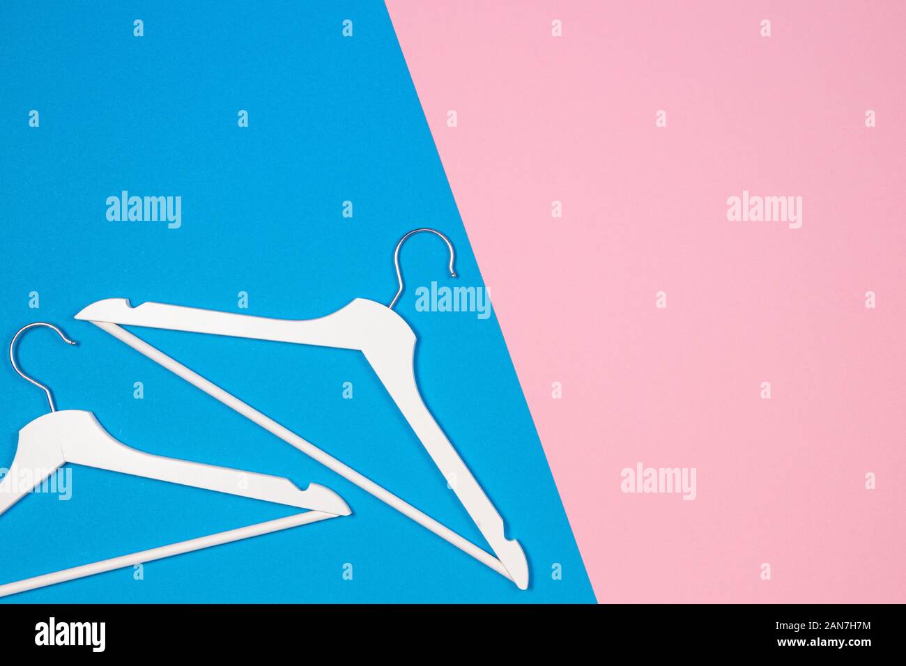 Two white wooden clothes hangers on pastel pink and blue background