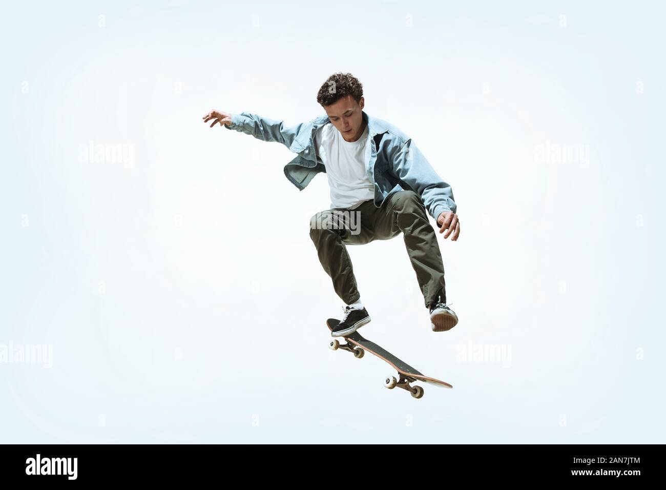 Caucasian young skateboarder riding isolated on a white studio background. Man in casual clothing training, jumping, practicing in motion. Concept of hobby, healthy lifestyle, youth, action, movement. Stock Photo