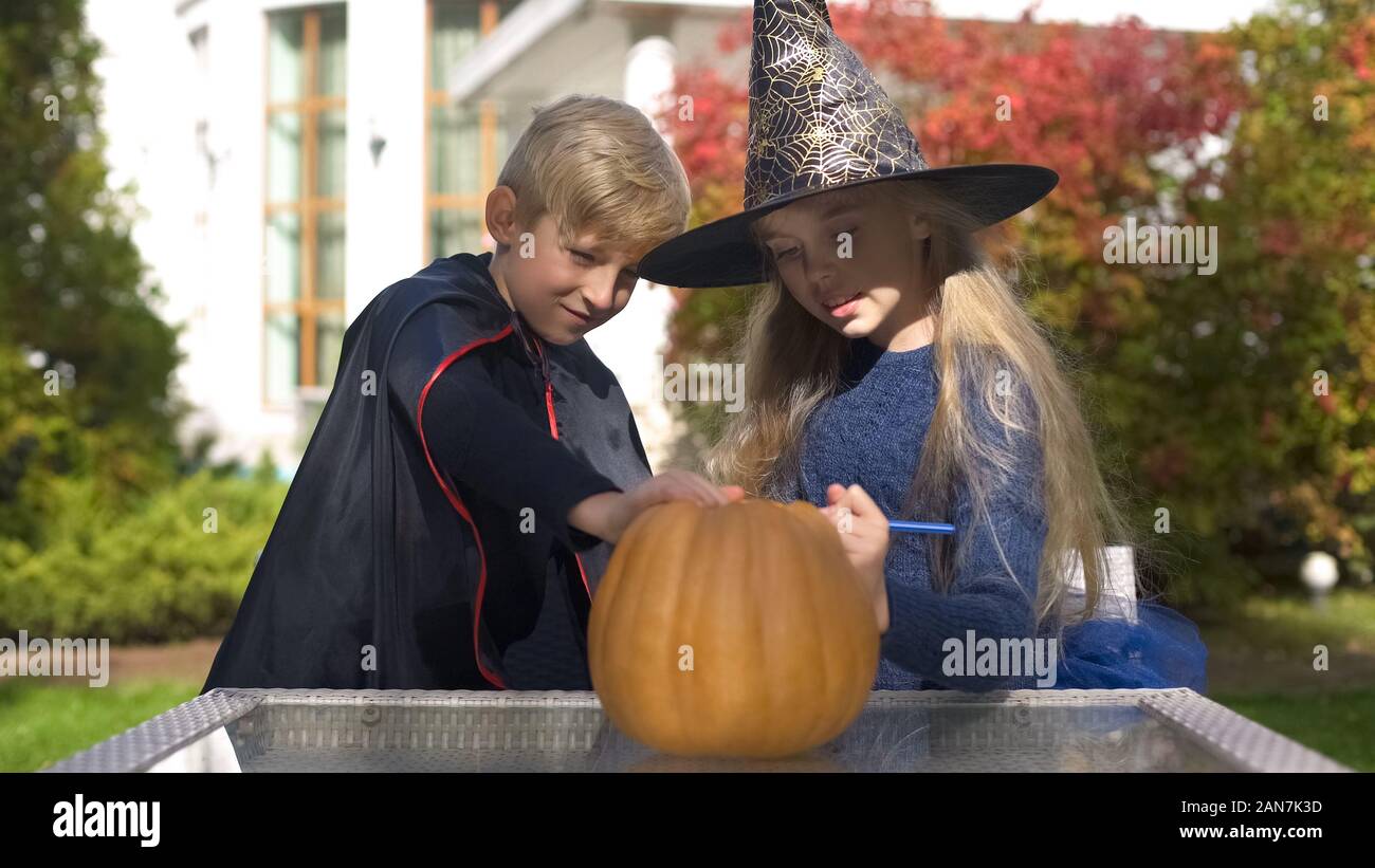 Little vampire and witch drawing scary face on pumpkin, preparing jack ...