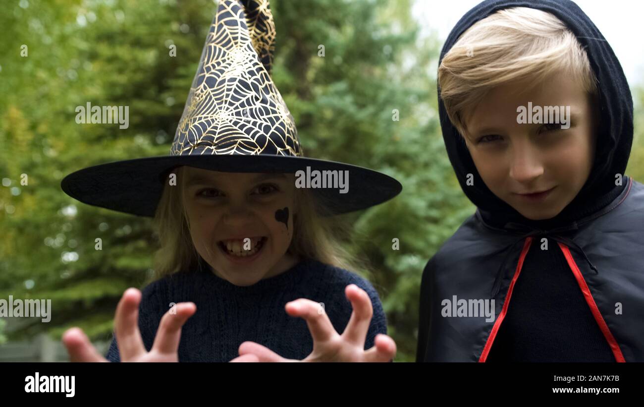 Girl in witch hat and boy in mantle chasing camera, growling spooky, Halloween Stock Photo