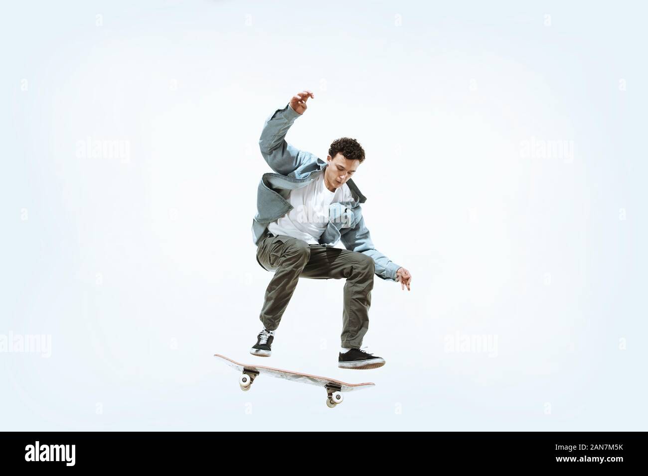Caucasian young skateboarder riding isolated on a white studio background. Man in casual clothing training, jumping, practicing in motion. Concept of hobby, healthy lifestyle, youth, action, movement. Stock Photo