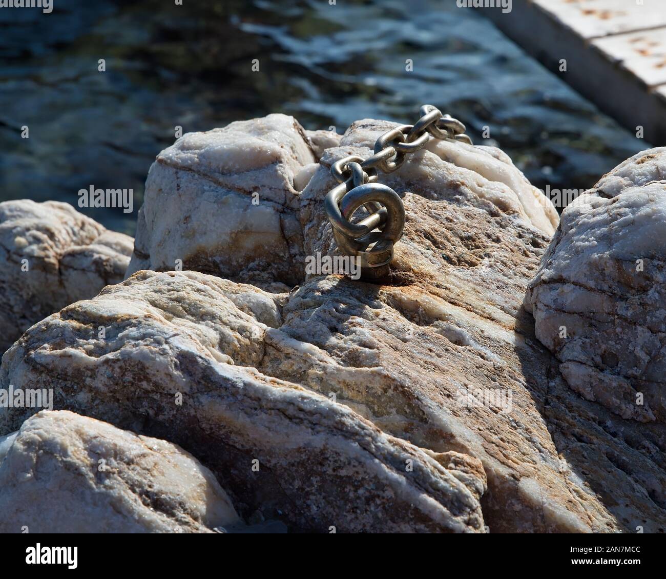 Rusted Heavy duty eye bolt with chain attached to beach rock . Stock Image Stock Photo