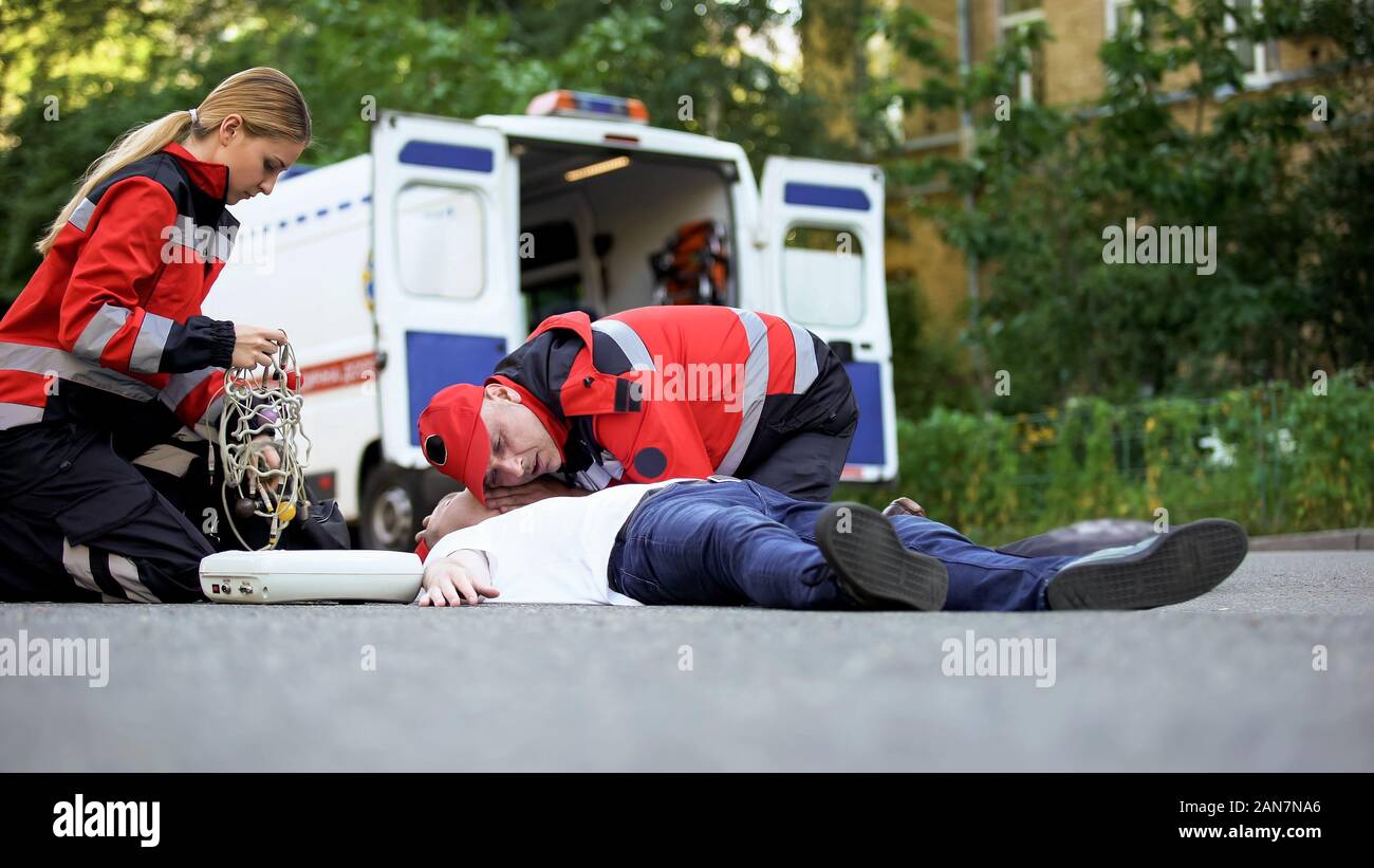Paramedics providing emergency medical care to man on road, car