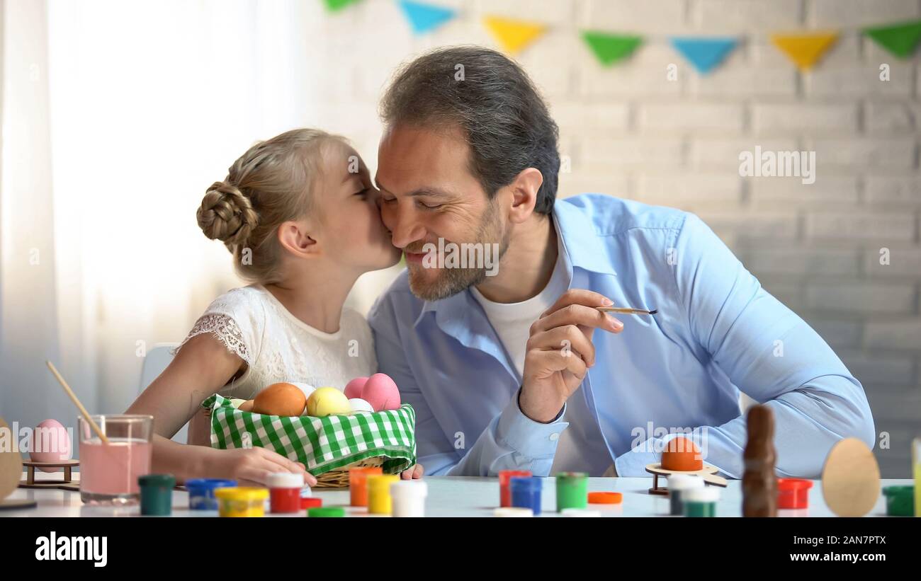 Loving daughter kissing father on cheek, painting eggs for Easter festival Stock Photo
