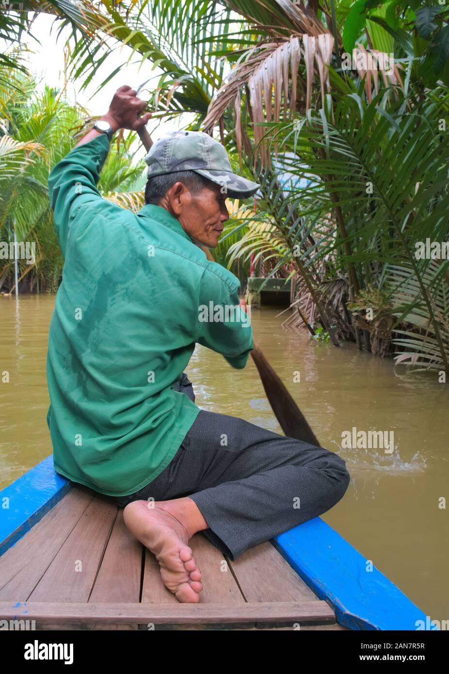 Vietnamese man on bare feet rowing on a boat along one of the ...