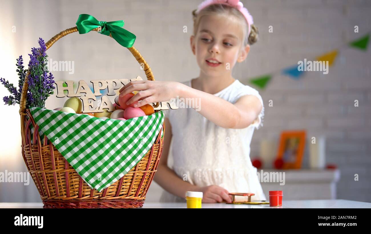 School girl putting colored egg in basket, holiday atmosphere, preparation Stock Photo