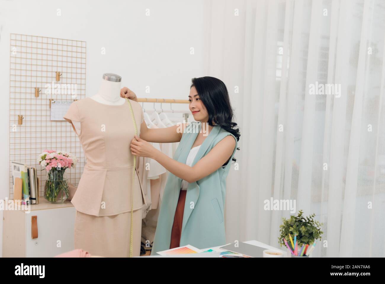 Young Asian female fashion designer taking measurements on mannequin in