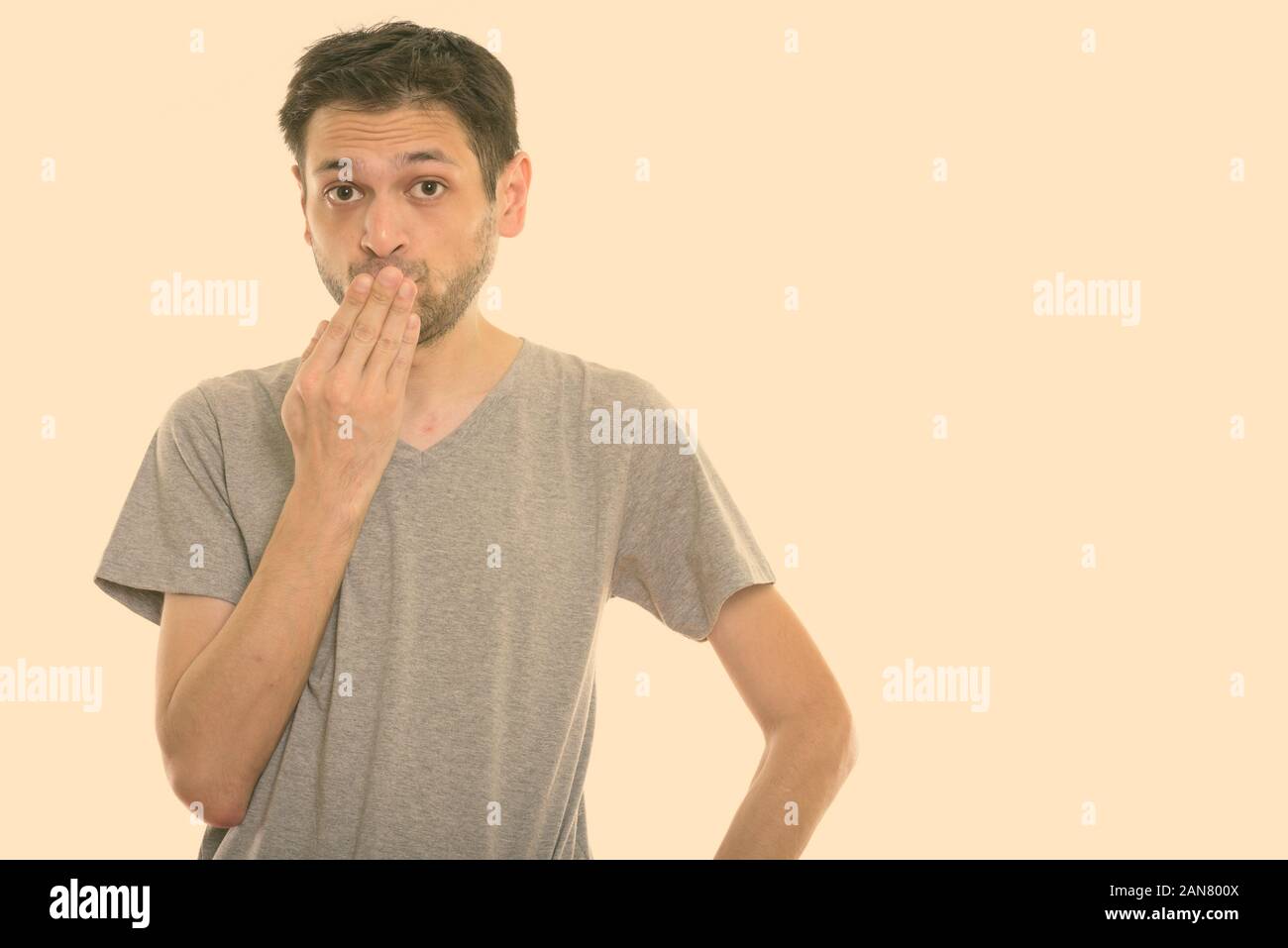 Studio shot of young man looking shocked while covering mouth Stock Photo