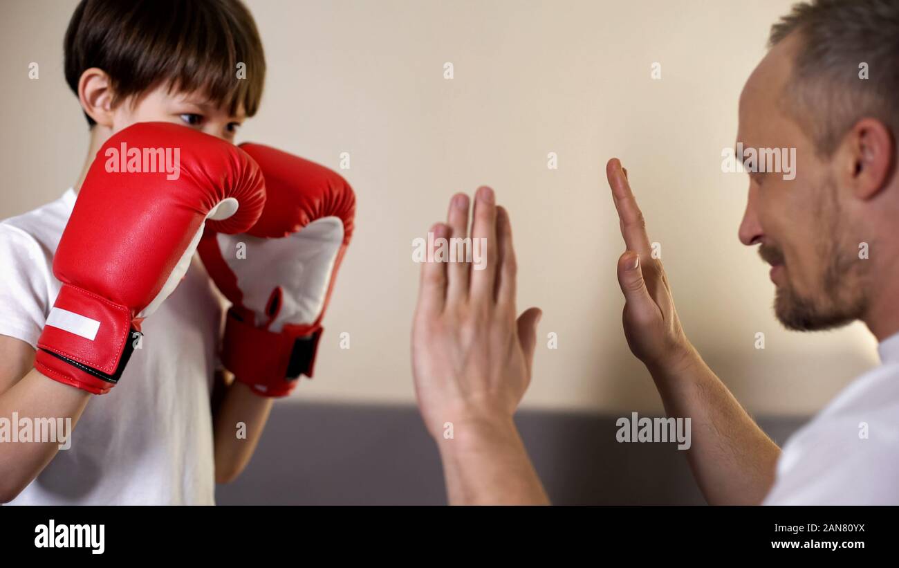 Cute kid practicing boxing punches with his coach, having fun with