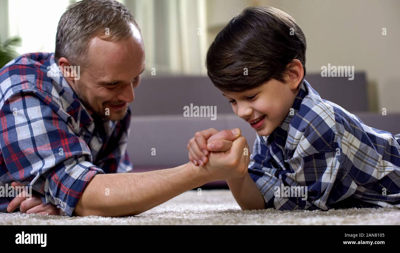 Cheerful father and son arm-wrestling on floor, having fun together ...
