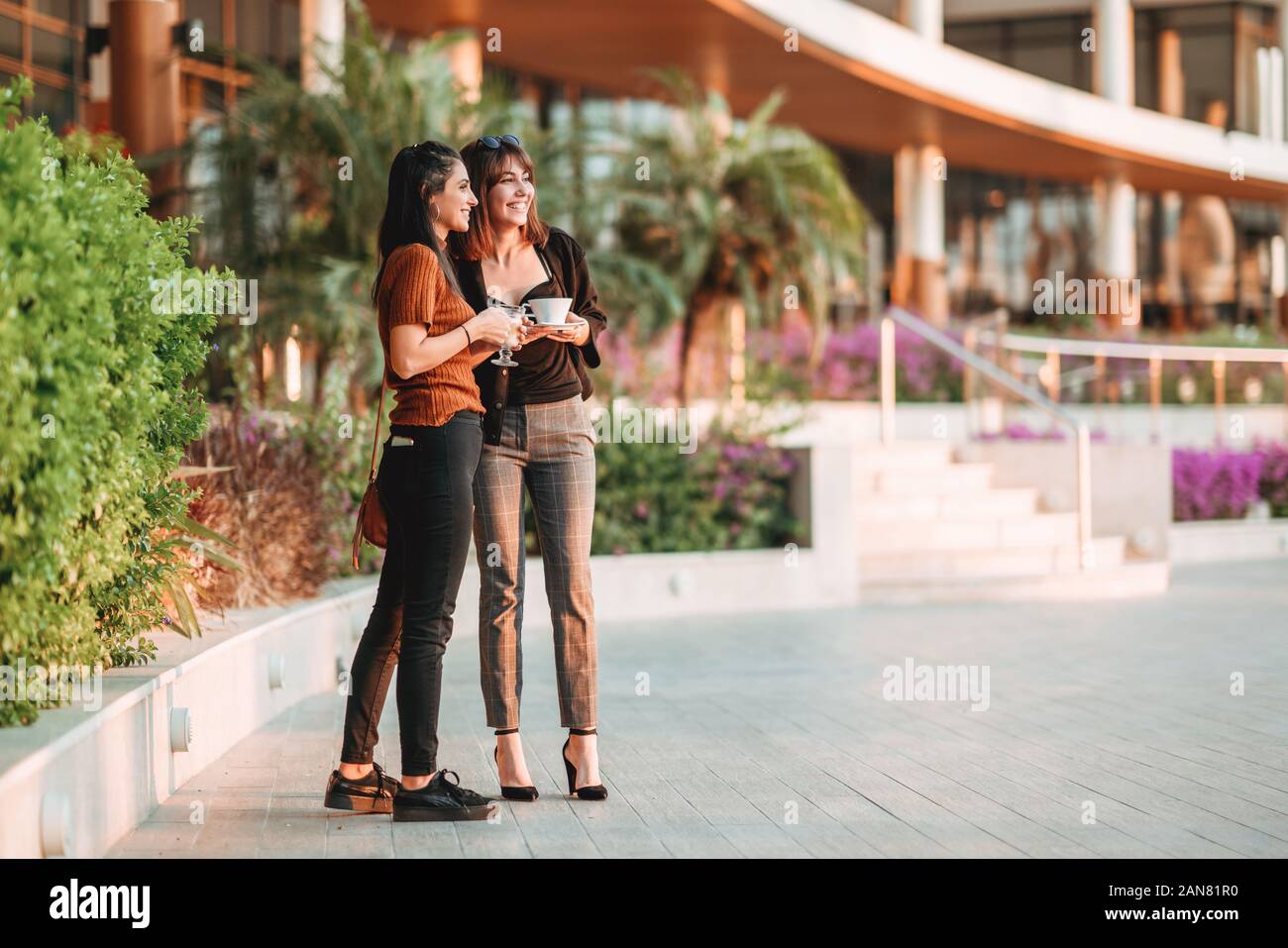 Two pretty women standing and talking with their drinks. Stock Photo