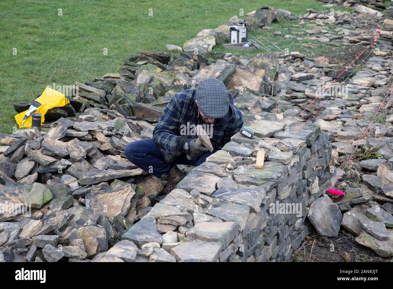 A dry stone wall craftsman restoring a dilapidated wall to its former glory on the boundary of a sports field in West Yorkshire, England U.K. Stock Photo