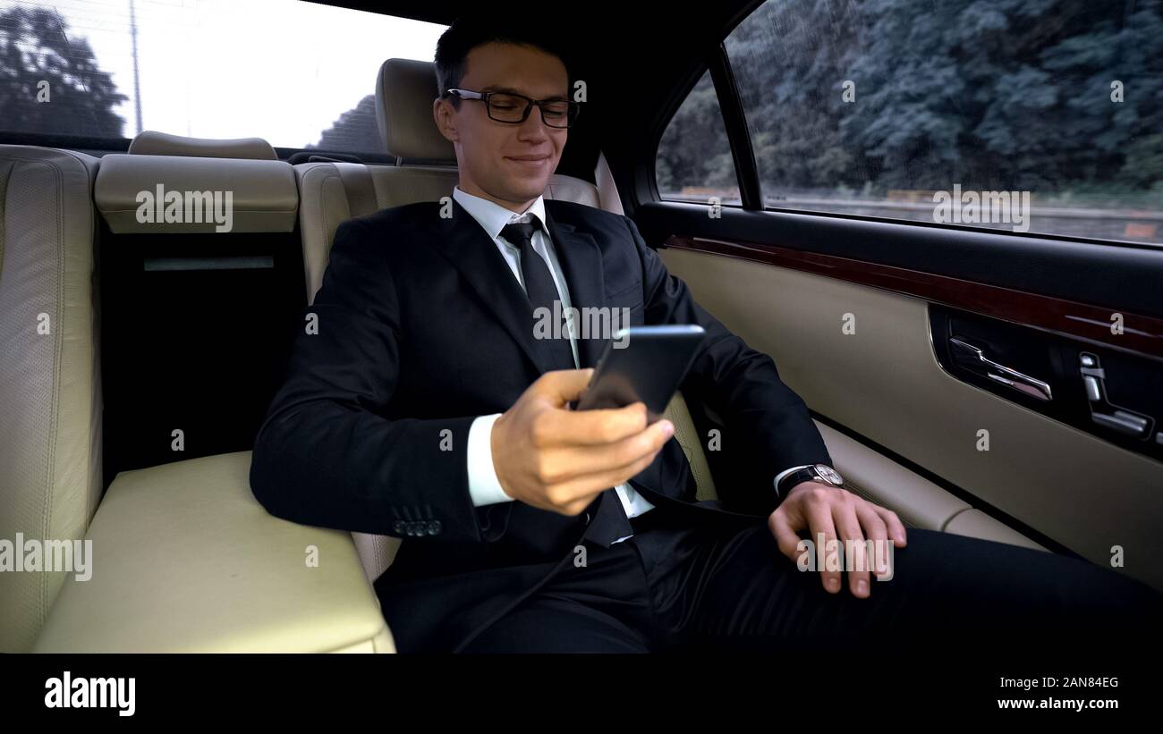 Delighted businessman riding on backseat of expensive car, using phone app Stock Photo