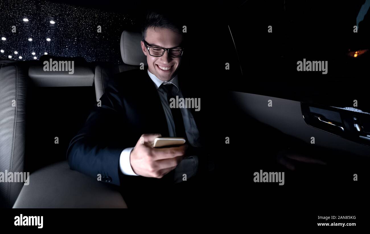 Male in suit texting with girlfriend on back seat of car as driving home, flirt Stock Photo