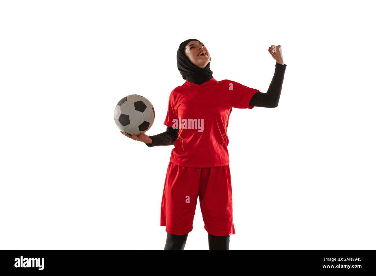 Emotions. Arabian female soccer or football player on white studio background. Young woman celebrating goal or match winning, catched in motion, action. Concept of sport, hobby, healthy lifestyle. Stock Photo
