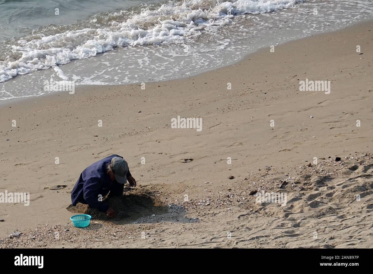 Pattaya, Thailand - December 23, 2019: Elder woman sitting on beach and trying to find clams. Stock Photo