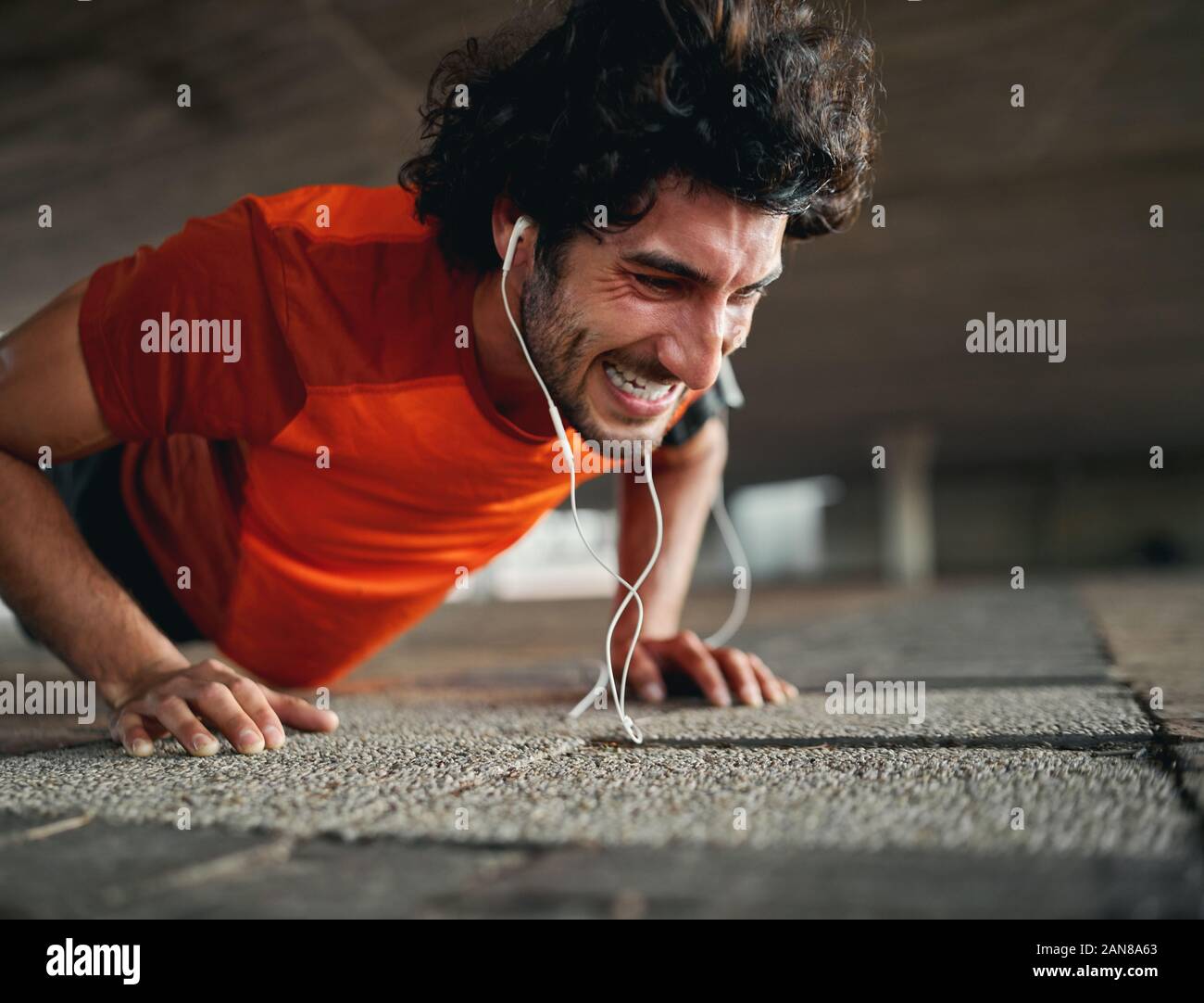 Young fit sporty man with serious face expression doing hard difficult plank fitness exercise or push ups on pavement Stock Photo